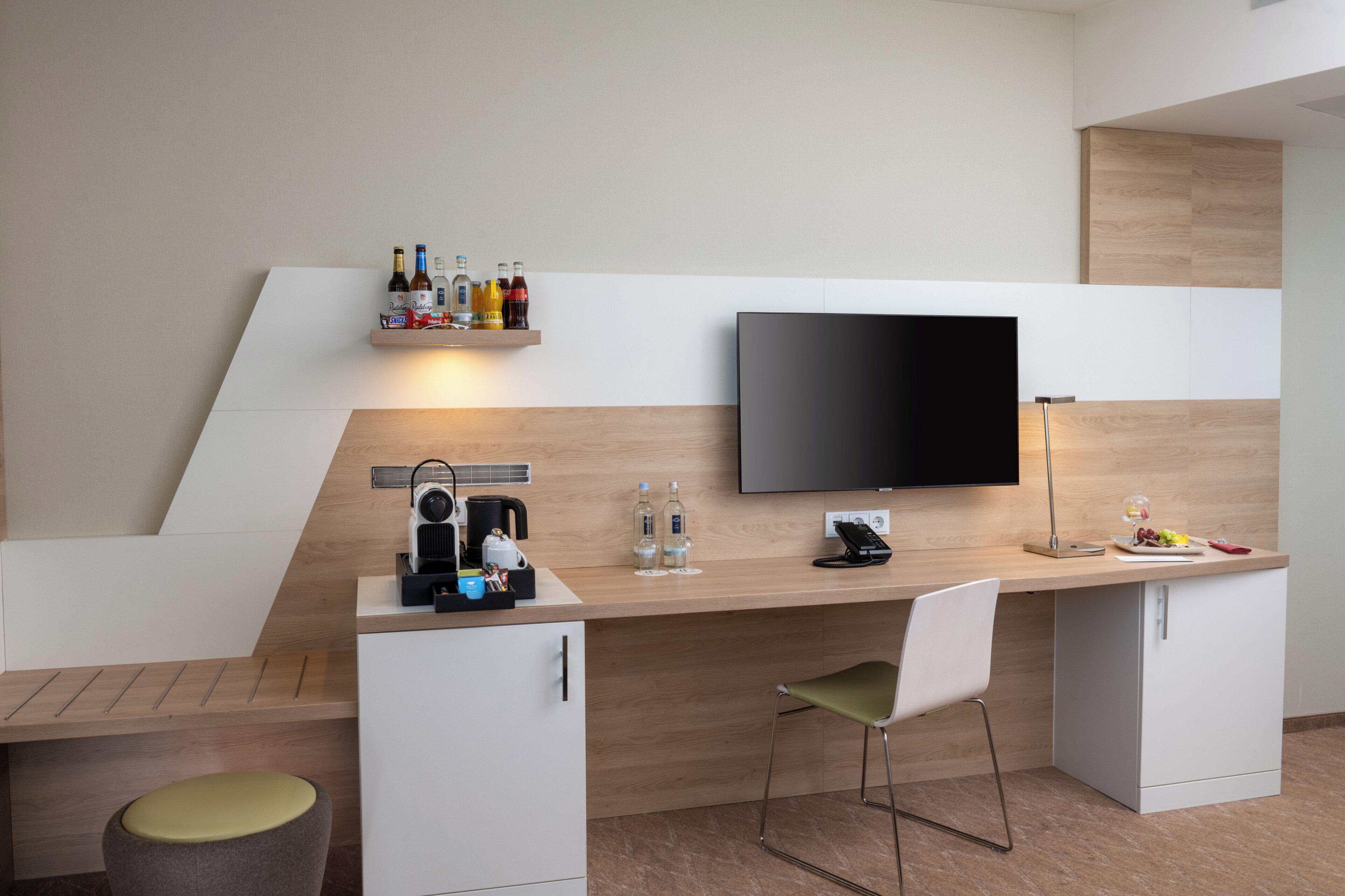 A modern kitchen with a flat-screen TV, a coffee maker, and a shelf with bottles.