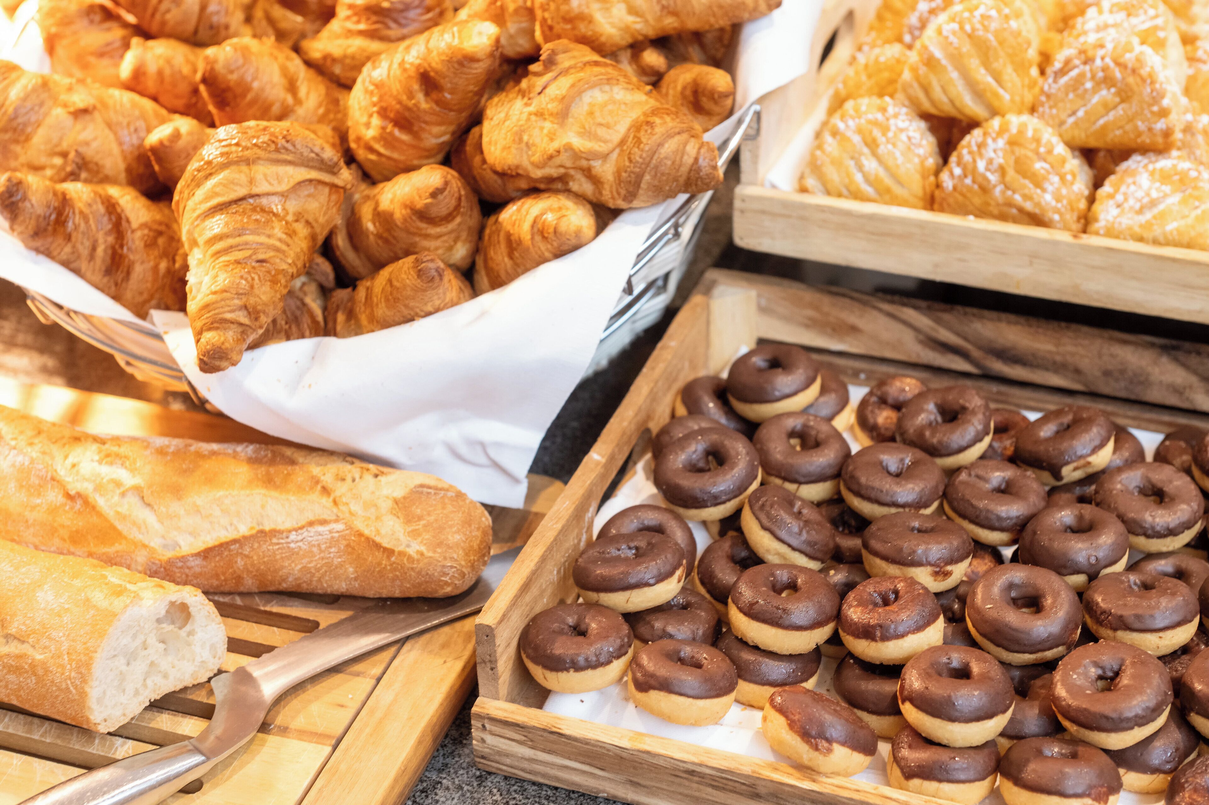 A variety of baked goods including croissants and chocolate donuts arranged on wooden trays.