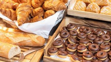 A variety of baked goods including croissants and chocolate donuts arranged on wooden trays.