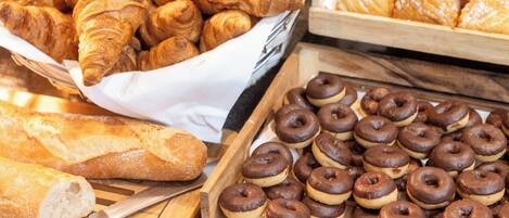 A variety of baked goods including croissants and chocolate donuts arranged on wooden trays.