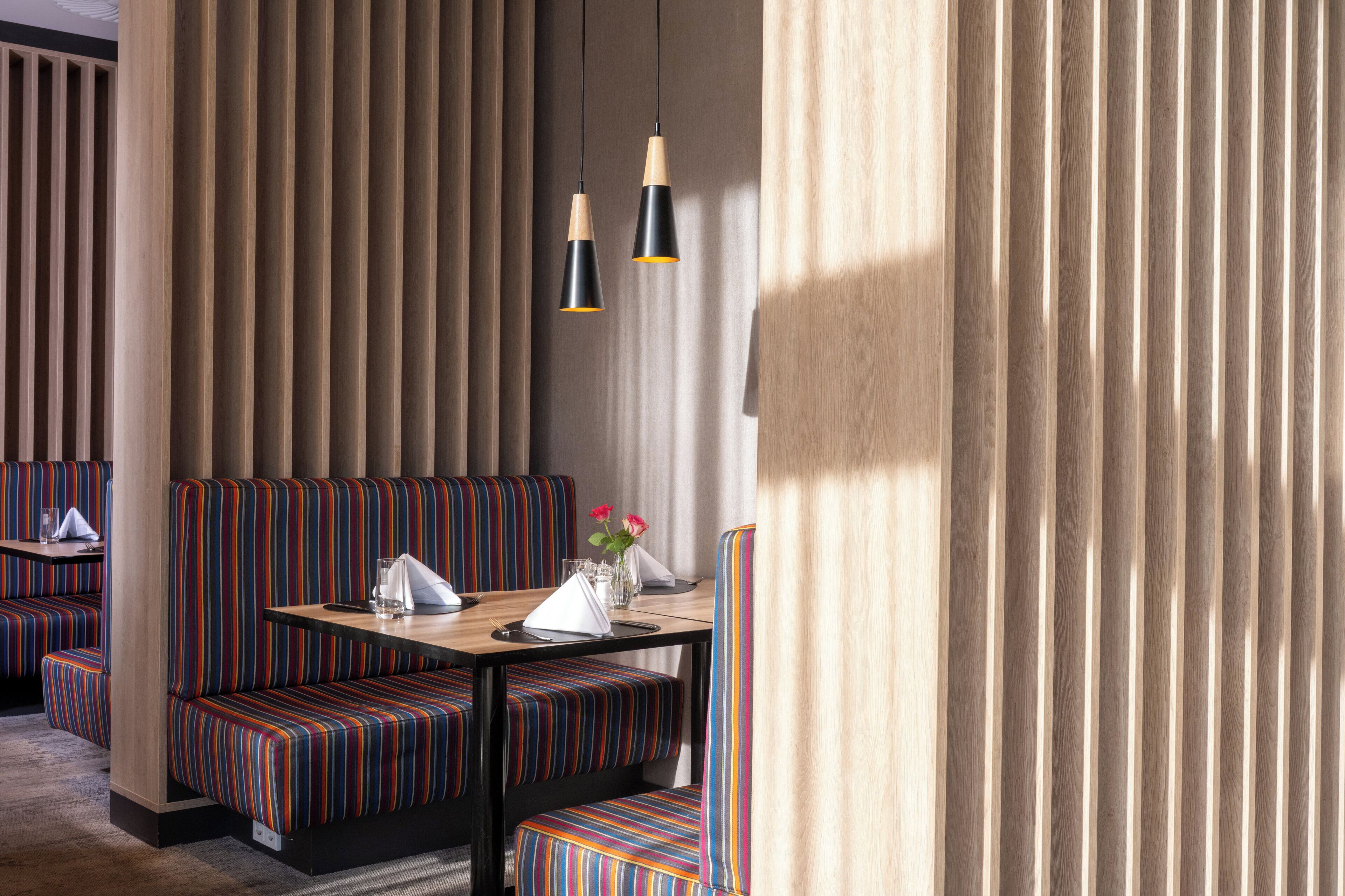 A restaurant with striped booth seating, a wooden table with a vase of flowers, and pendant lighting.