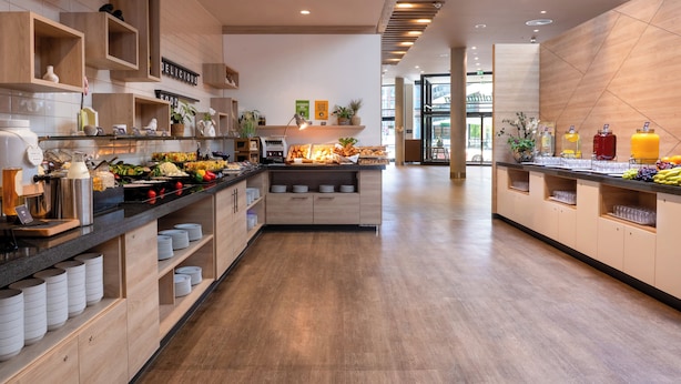 A modern hotel kitchen with wooden cabinetry, a buffet counter, and a variety of food items.