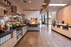 A modern hotel kitchen with wooden cabinetry, a buffet counter, and a variety of food items. - Holiday Inn Frankfurt Airport by IHG (Frankfurt)
