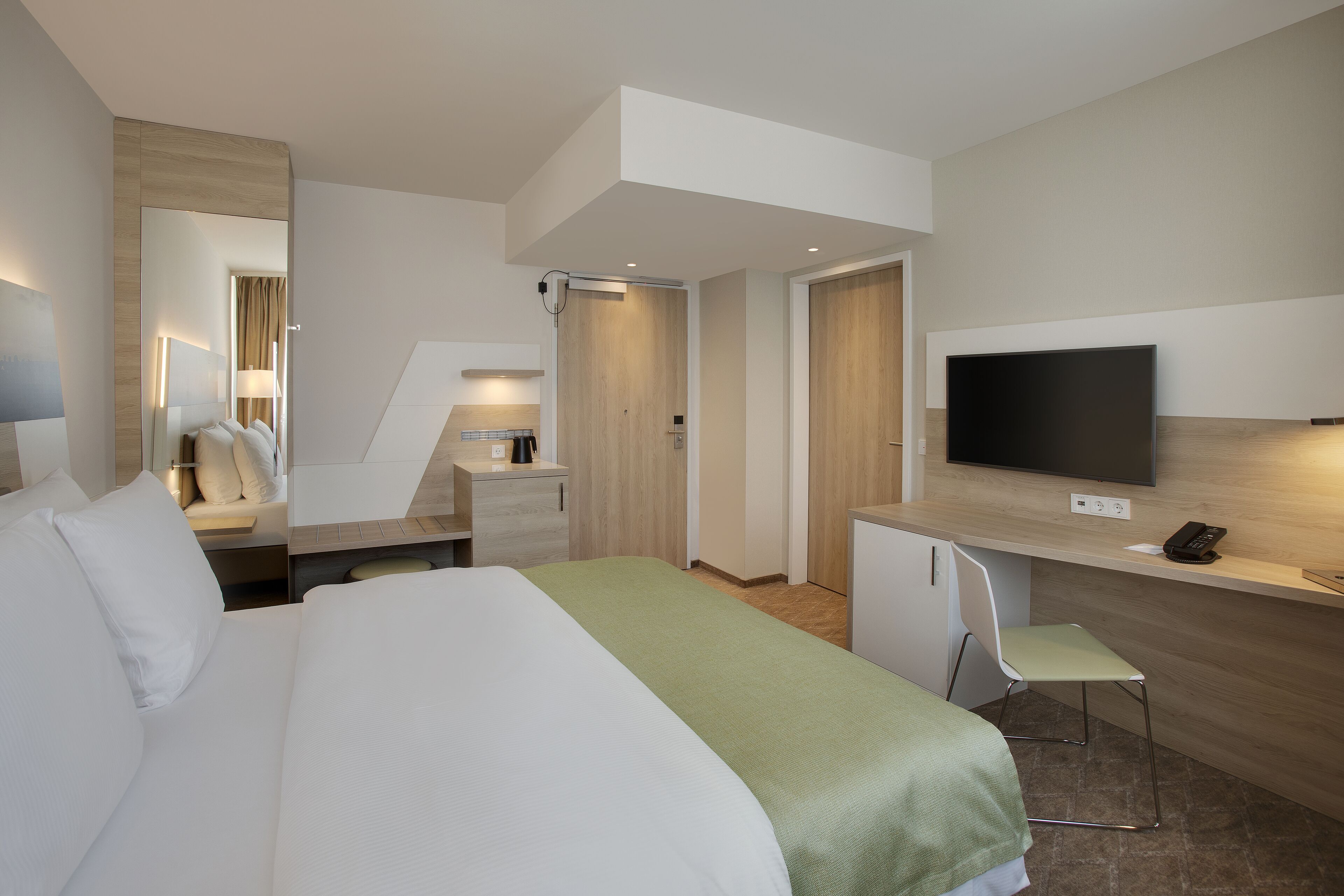 A modern hotel room with a large bed, a desk, a television, and a small chair.