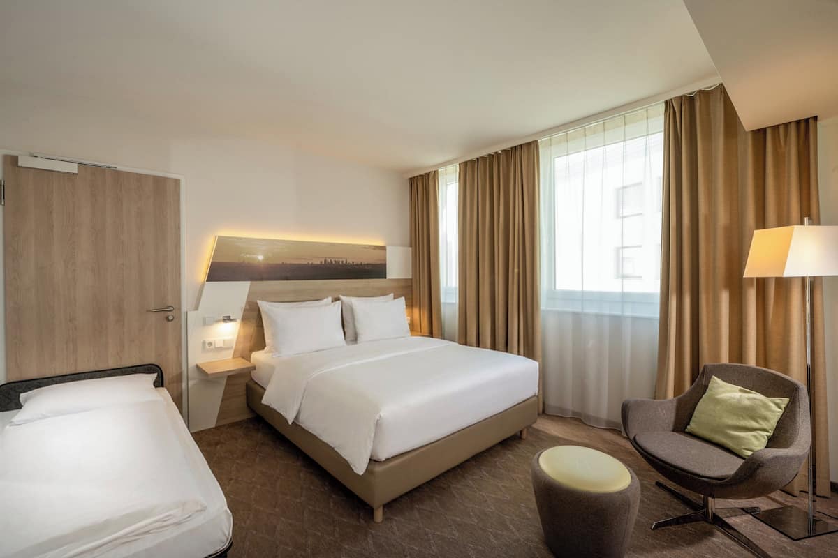 A hotel room with a bed, a chair, a nightstand, and a lamp.
