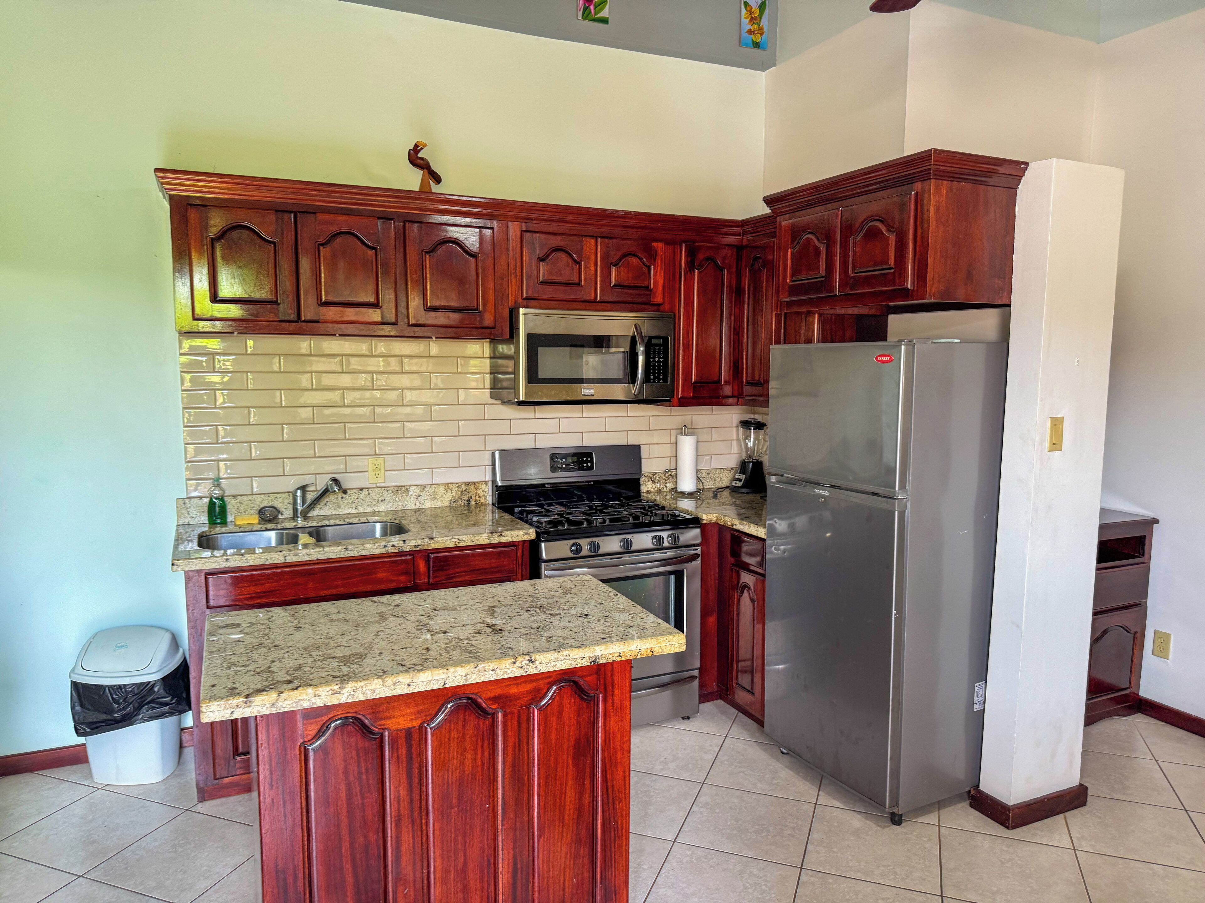 A kitchen with wooden cabinets, a stainless steel refrigerator, a microwave, and a stove.