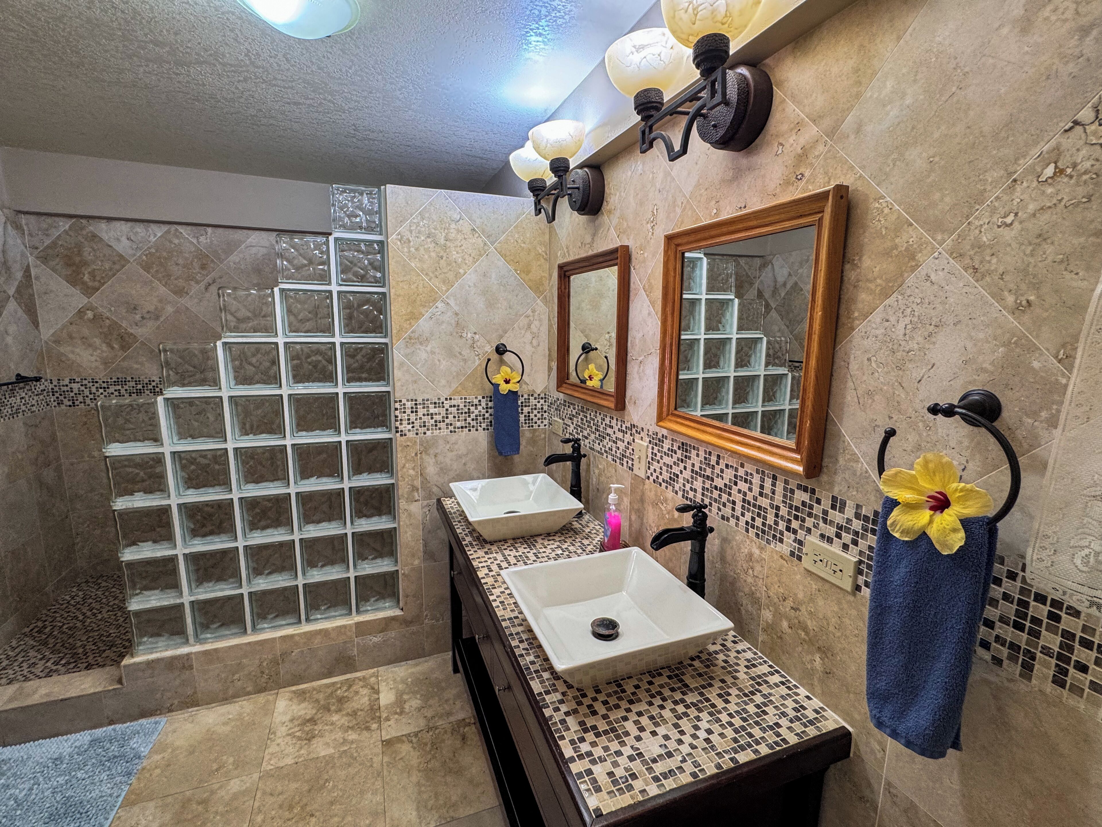 A bathroom with a glass shower enclosure, a sink with a mirror, and a towel rack with a flower.