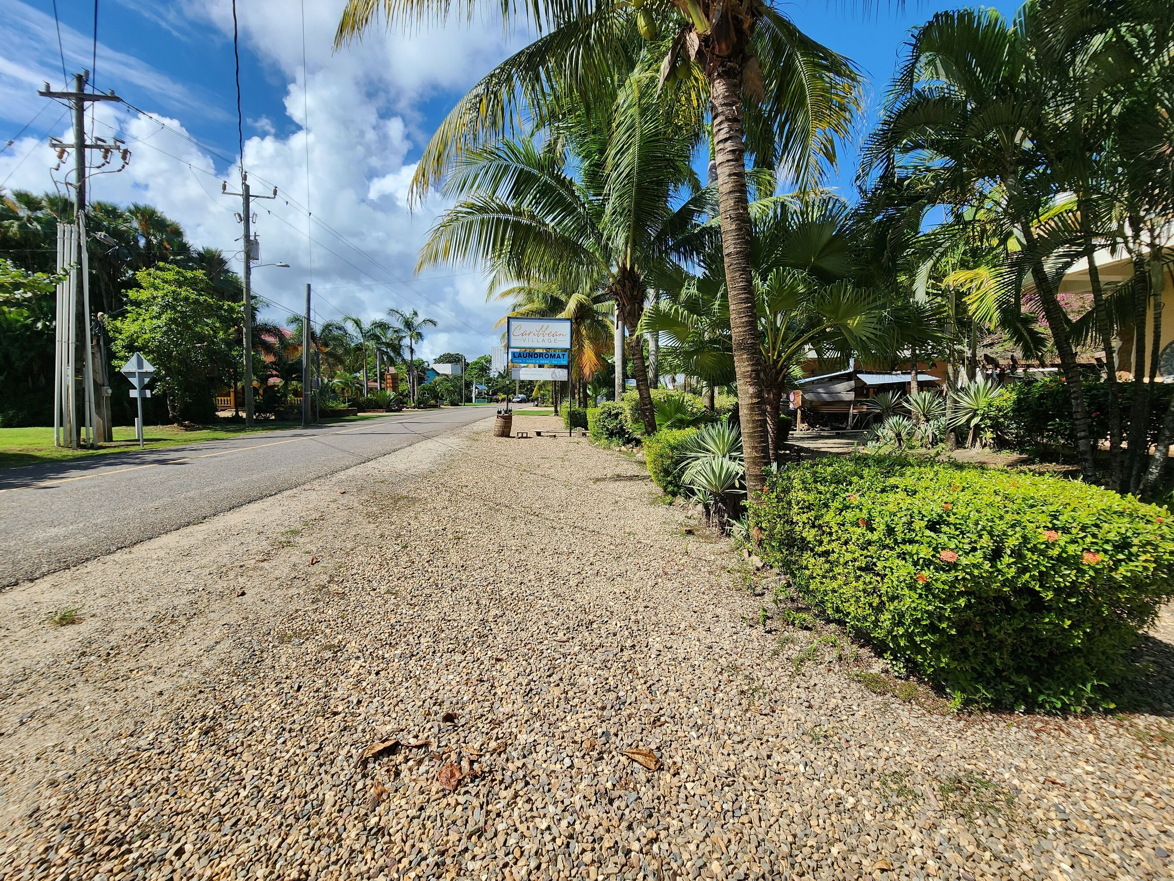 Een grindweg met palmbomen en een bordje voor Caribbean Village Laundromat.
