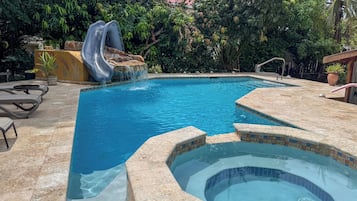 Una piscina con tobogán, jacuzzi y sillas de descanso.