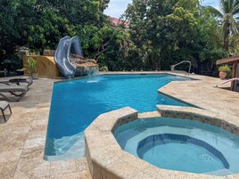 Una piscina con tobogán, jacuzzi y sillas de descanso.