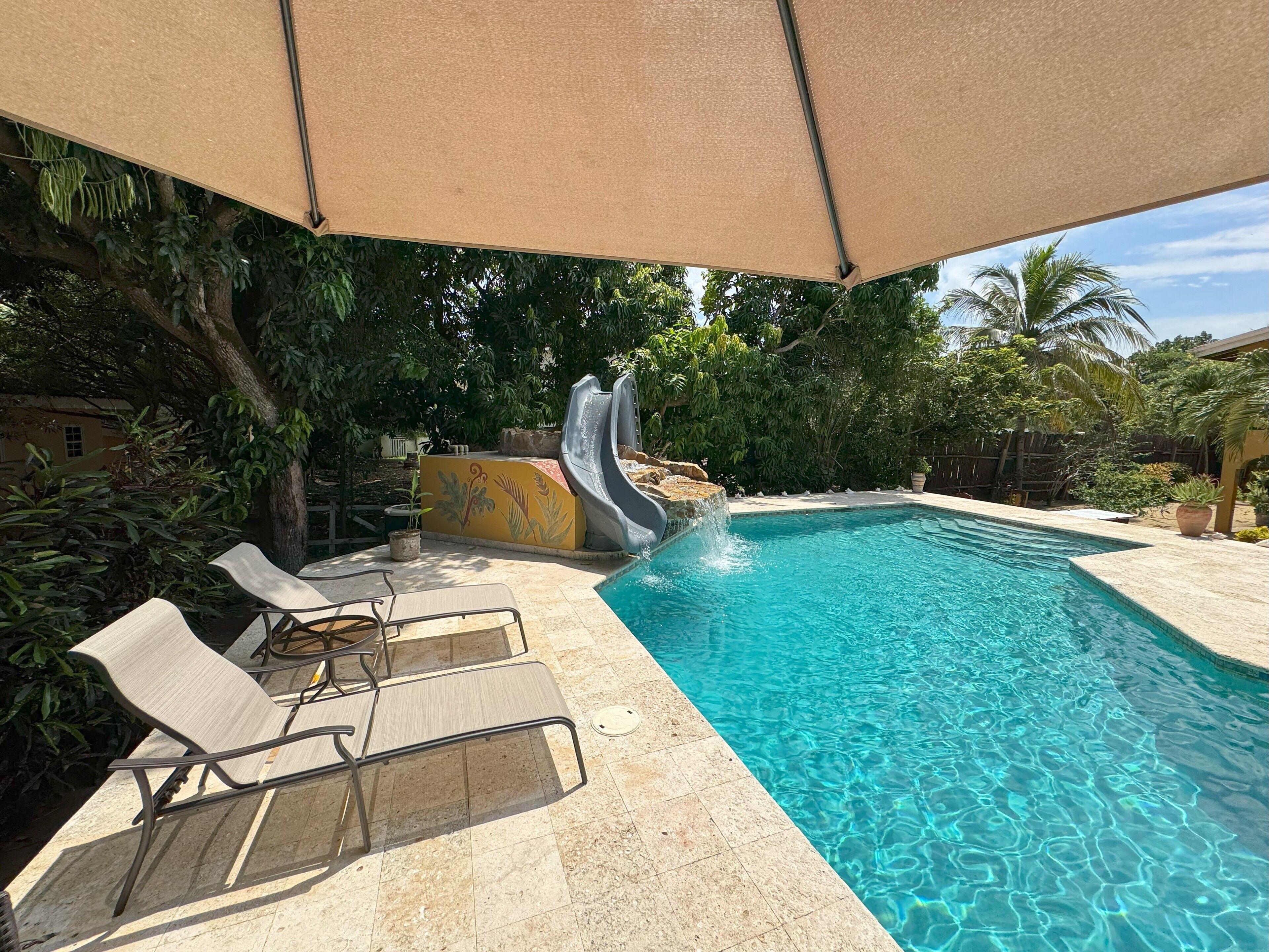 Une piscine avec un toboggan, des chaises longues et un espace ombragé.