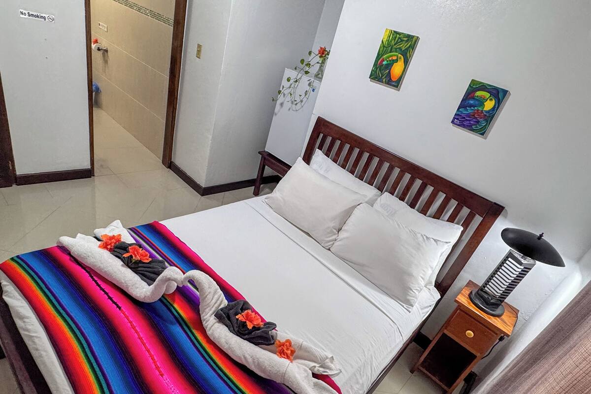 A hotel room with a bed, a bedside table with a lamp, and two wall art pieces.