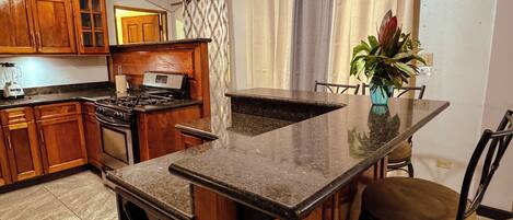 A kitchen with wooden cabinets, a stove, and a dining area with chairs and a table.