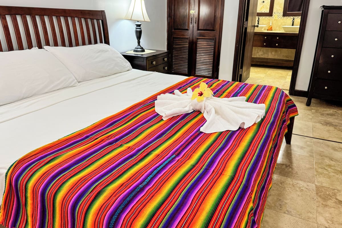 A hotel room with a neatly made bed, a bedside lamp, a wooden wardrobe, and a bathroom visible through an open door.