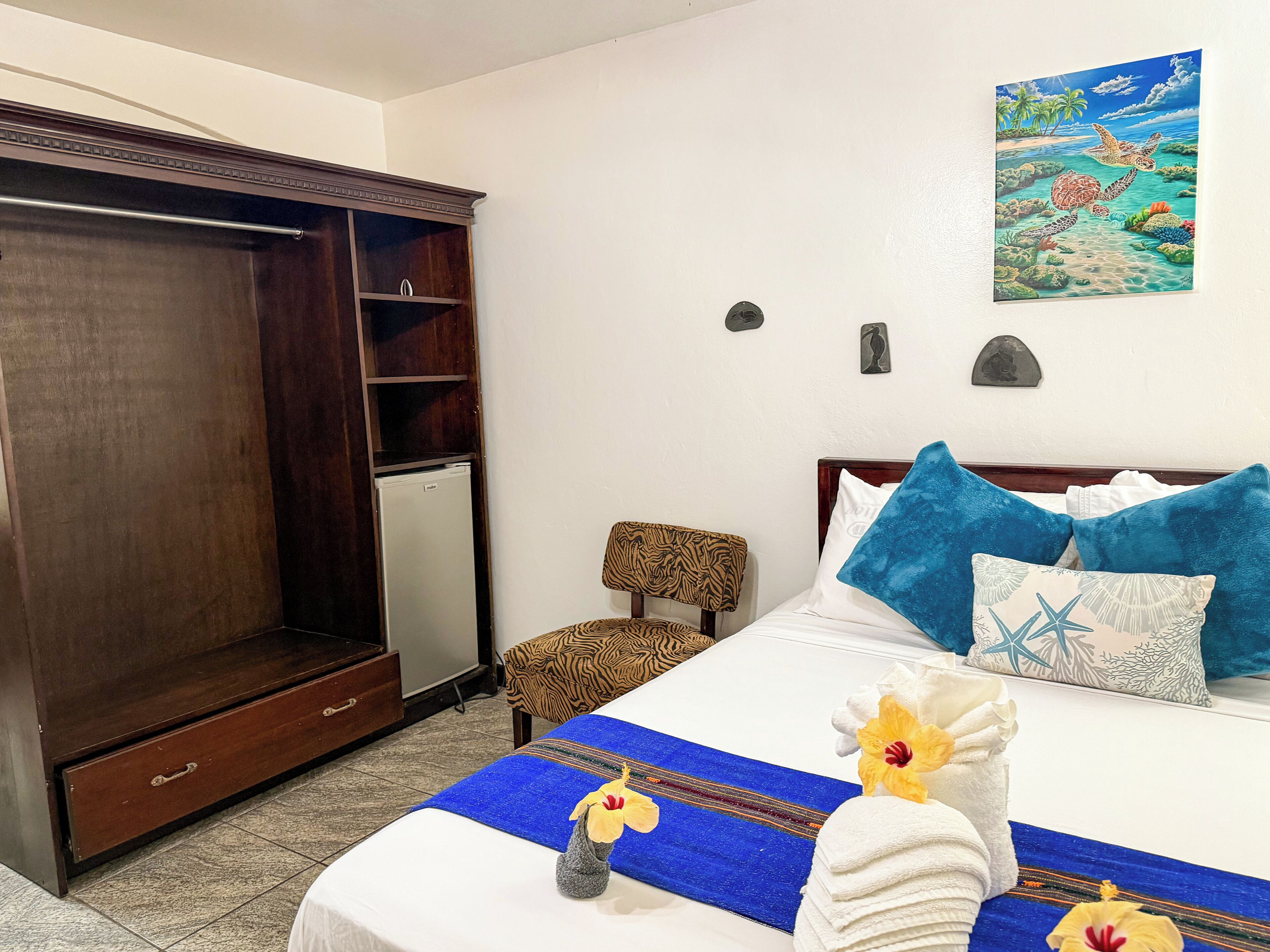 A hotel room with a bed, a wardrobe, a chair, and a painting on the wall.