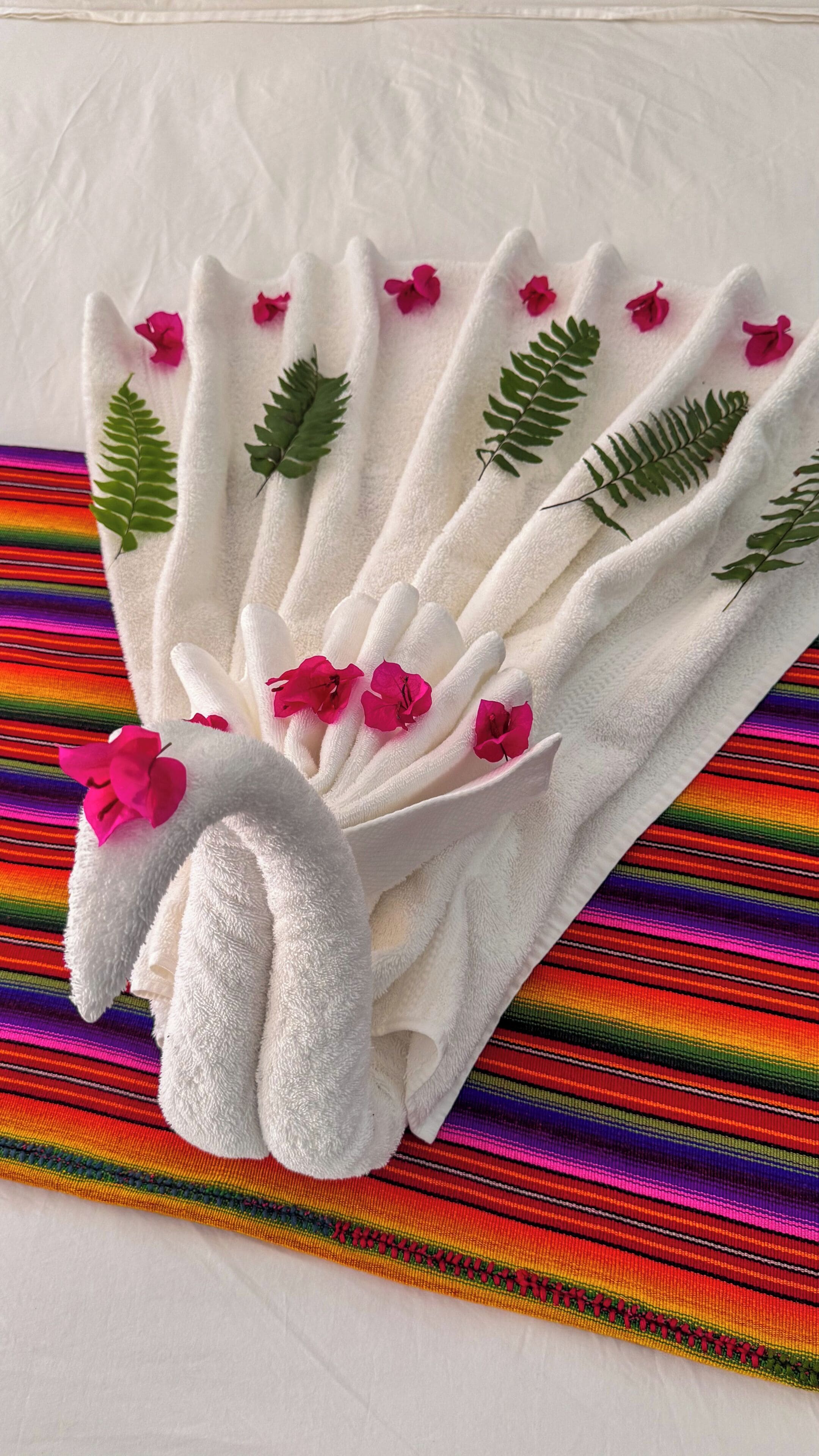 A white towel with pink flowers and green leaves, placed on a colorful striped fabric.