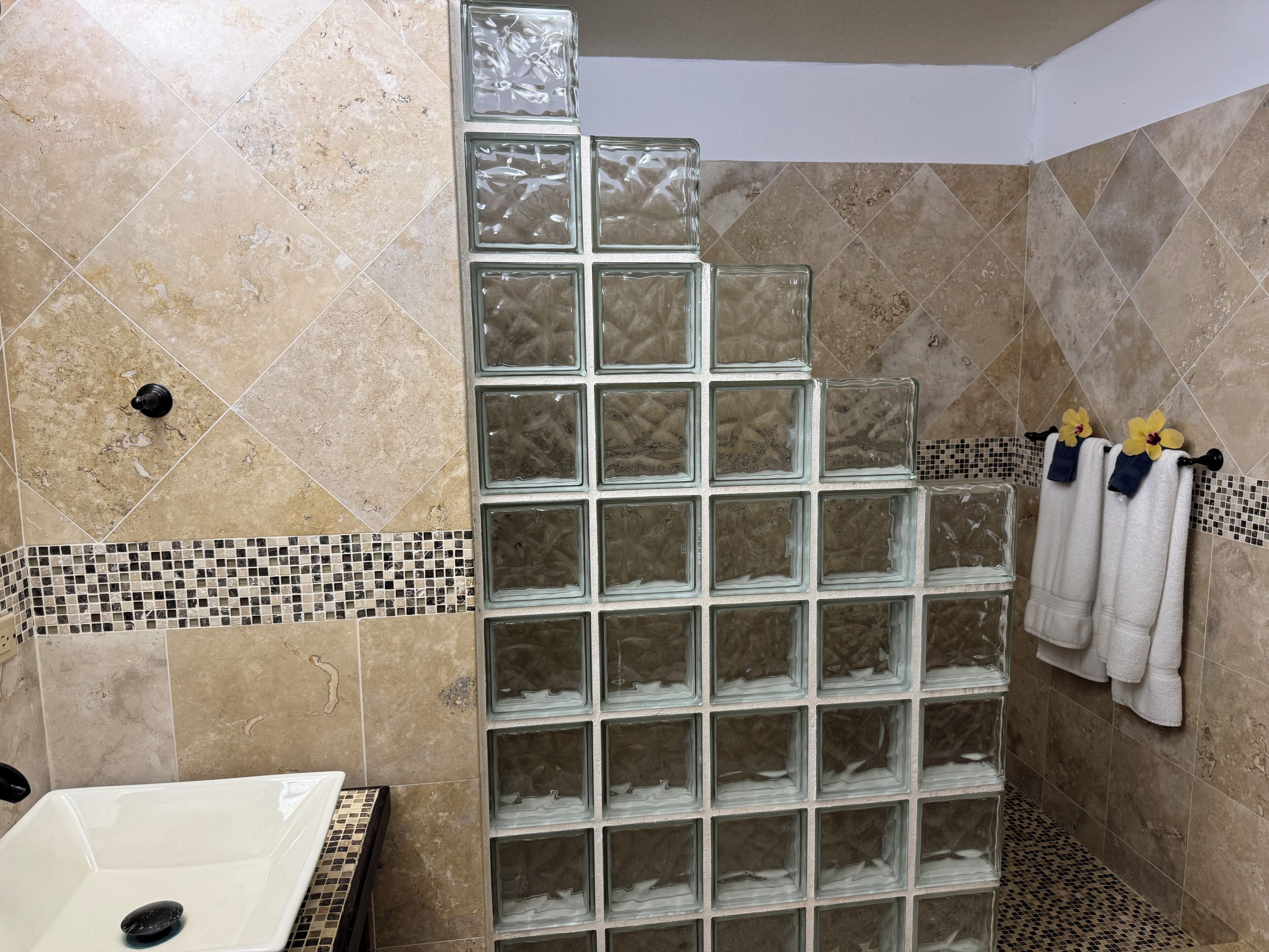 Un bagno con cabina doccia in vetro, una vasca da bagno bianca e pareti rivestite di piastrelle con una fascia a mosaico.