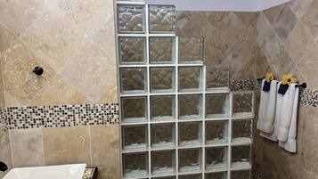 Un bagno con cabina doccia in vetro, una vasca da bagno bianca e pareti rivestite di piastrelle con una fascia a mosaico.