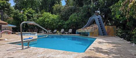 Una piscina amb tobogan, gandules i un mur de pedra.