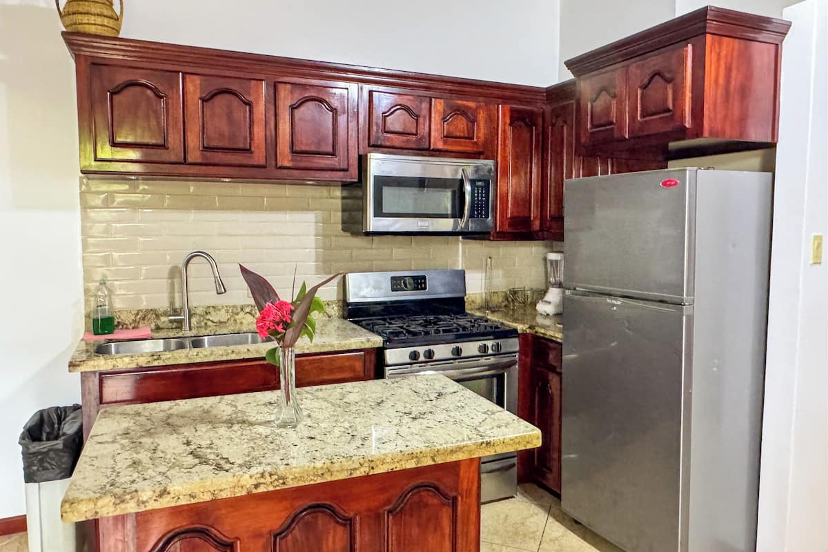 A kitchen with wooden cabinets, a granite countertop, a stainless steel refrigerator, a microwave, a stove, and a sink.