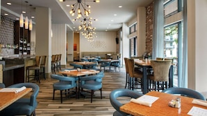 Un restaurant moderne avec des tables en bois et des chaises bleues, un coin bar avec des bouteilles et un grand lustre.