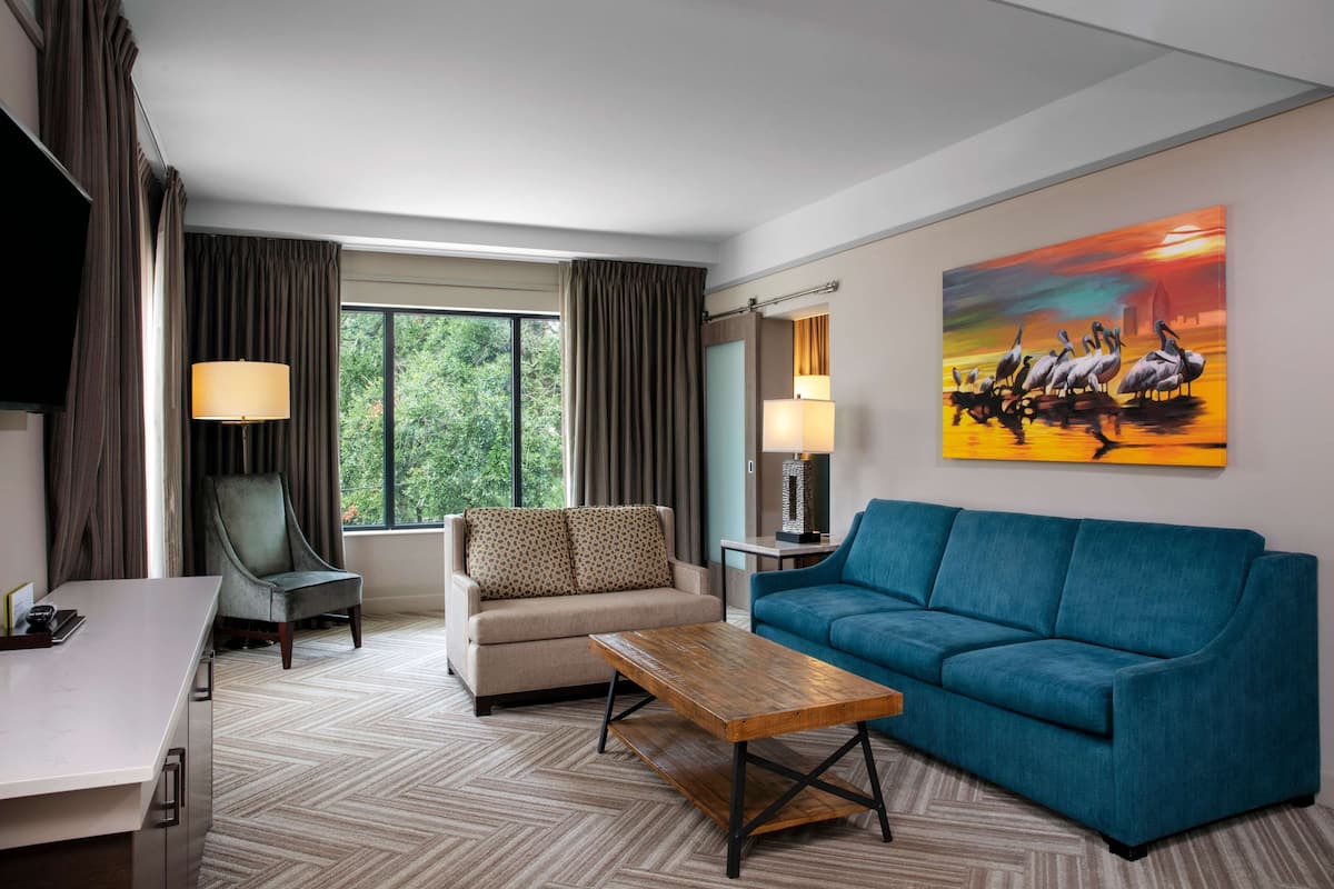 A hotel room with a sofa, armchair, coffee table, and a painting of birds.