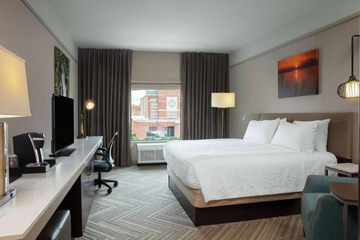 A hotel room with a bed, desk, chair, and a window with curtains.