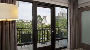 Une chambre d’hôtel avec un balcon comprenant une table et des chaises, une vue sur le paysage urbain et une grande fenêtre avec des rideaux.