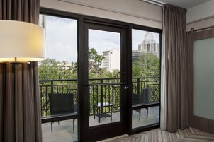Habitación de hotel con balcón que incluye una mesa y sillas, vistas a la ciudad y un amplio ventanal con cortinas.