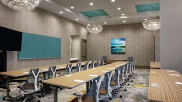 A conference room with long tables, chairs, and a projector screen.