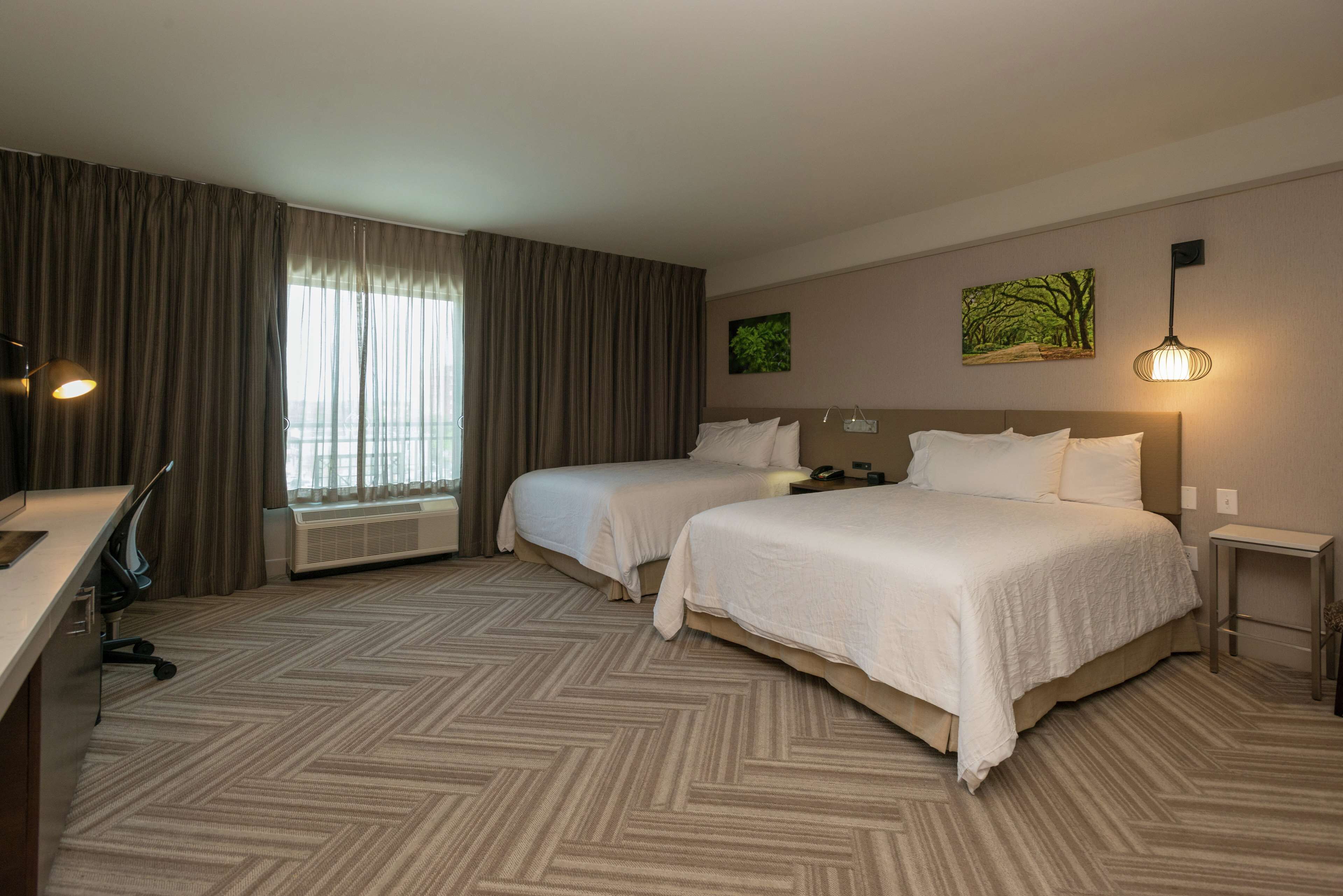 Une chambre d’hôtel avec deux lits, un bureau, une chaise, une lampe et un tableau au mur.