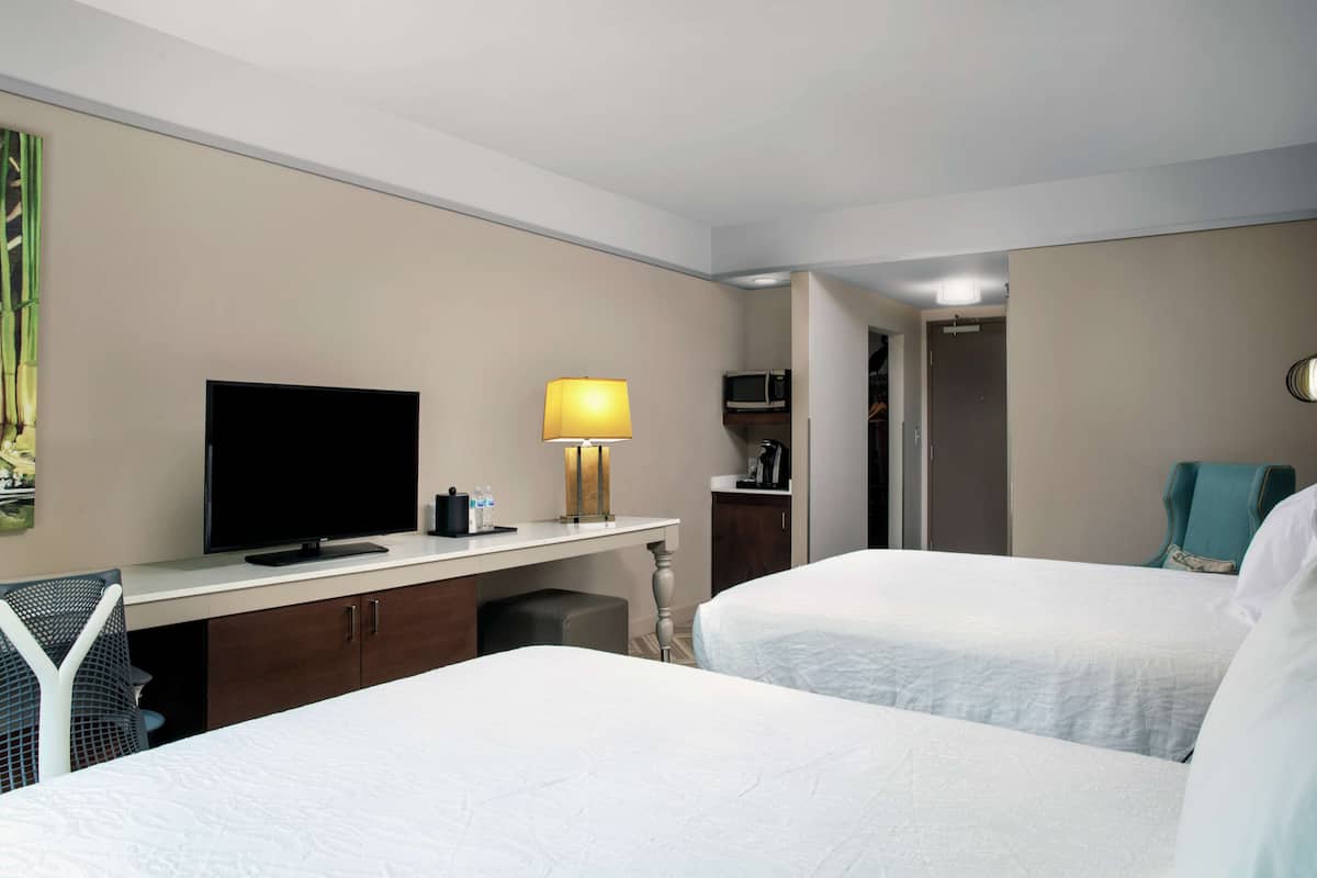 A hotel room with two beds, a desk with a TV, a lamp, and a microwave.