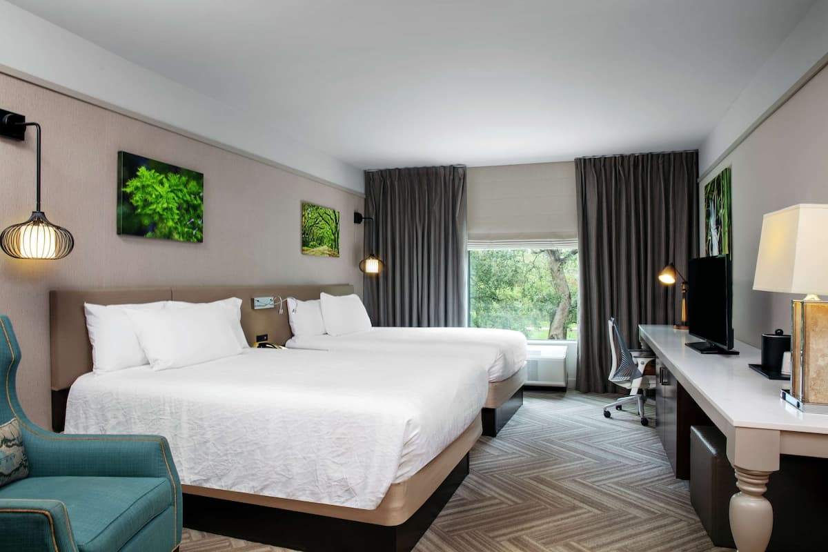 A hotel room with two beds, a desk, a chair, and a TV.