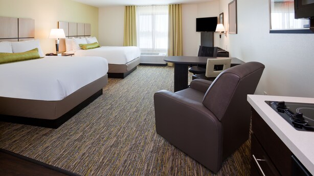 A hotel room with two beds, a desk, a chair, a TV, and a flat-screen TV mounted on the wall.