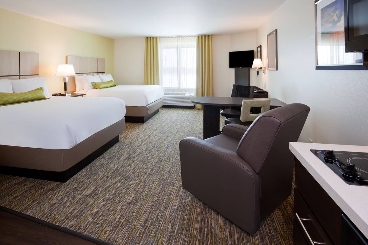 A hotel room with two beds, a desk, a chair, a TV, and a flat-screen TV mounted on the wall.