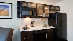 A compact kitchen with dark cabinetry, a dishwasher, a refrigerator, and a coffee maker.
