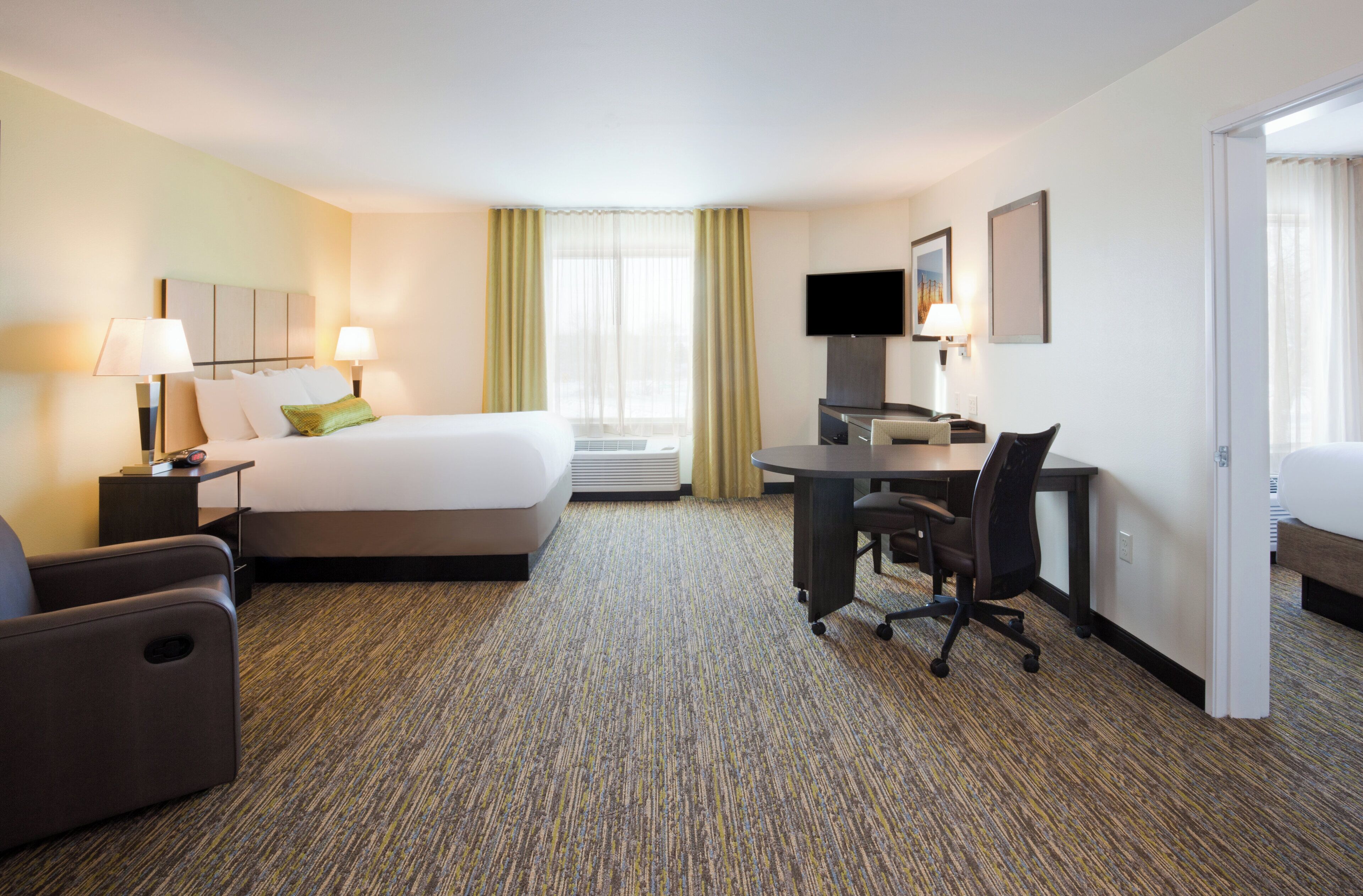 A hotel room with a bed, desk, chair, and a television.