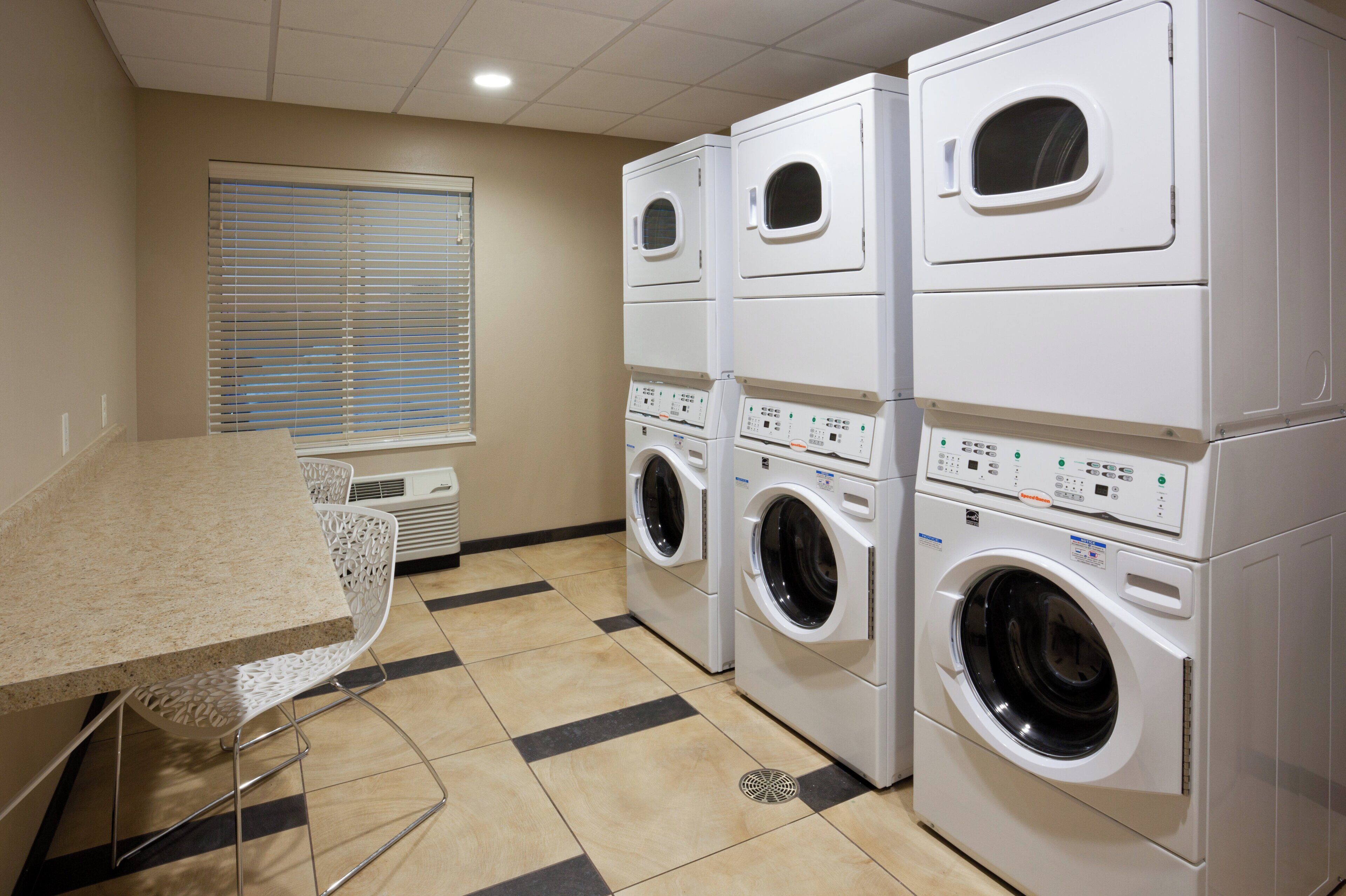 A laundry room with stacked washing machines, a table, and chairs.