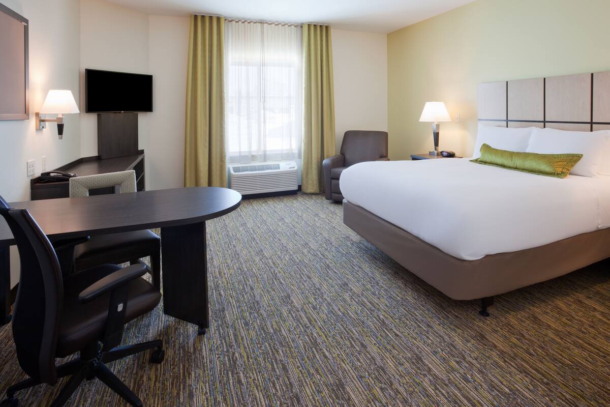 A hotel room with a bed, desk, chair, television, and air conditioning unit.