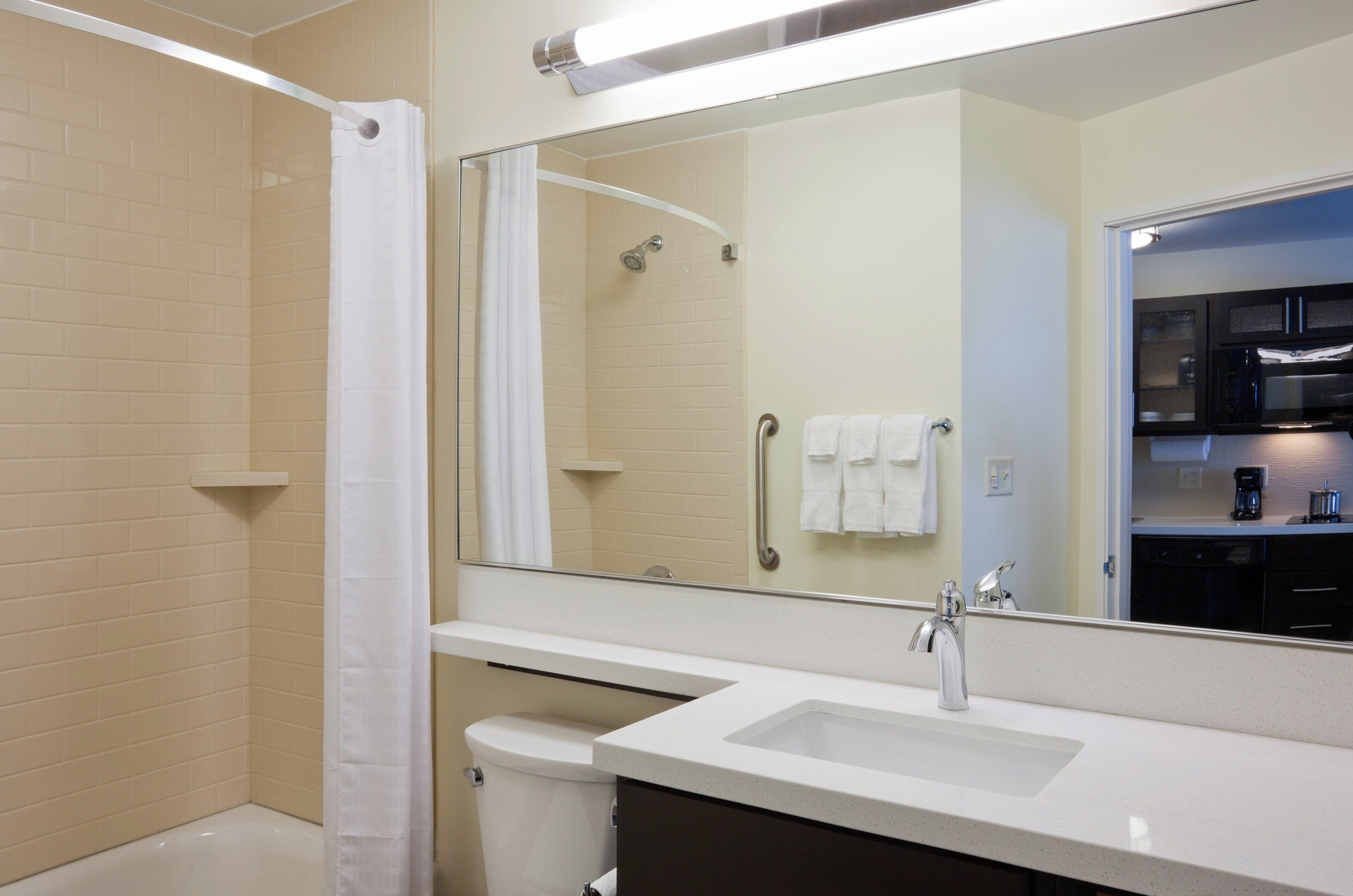 Un baño moderno con ducha, inodoro, lavamanos y un espejo grande que refleja la habitación.