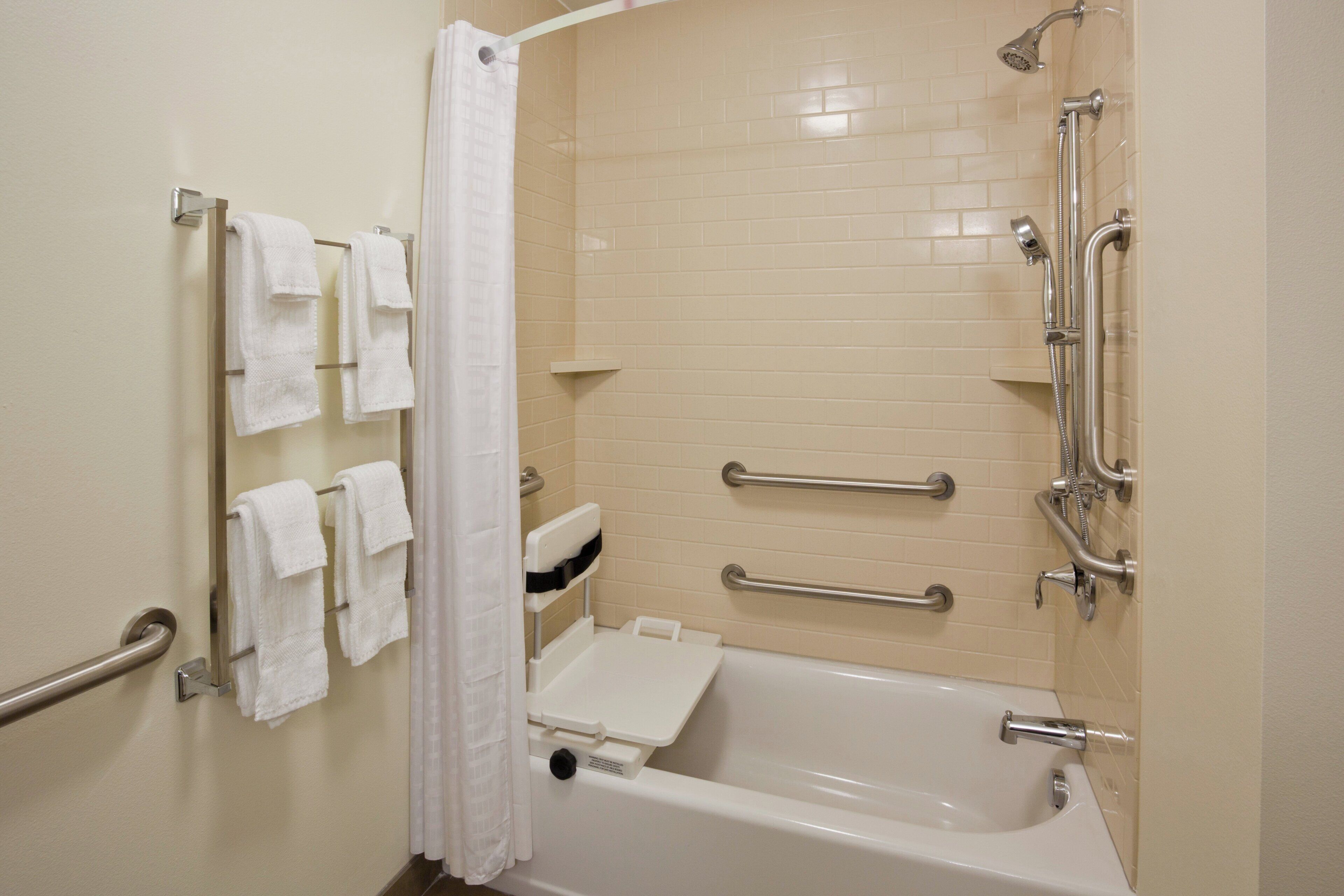 A bathroom with a bathtub, grab bars, a showerhead, and a towel rack.