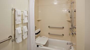 A bathroom with a bathtub, grab bars, a showerhead, and a towel rack.