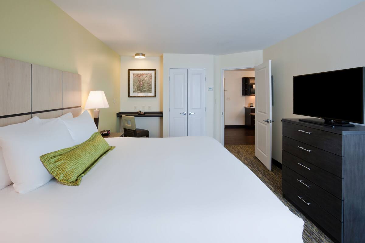 A hotel room with a large bed, a TV, a dresser, and a desk with a chair.