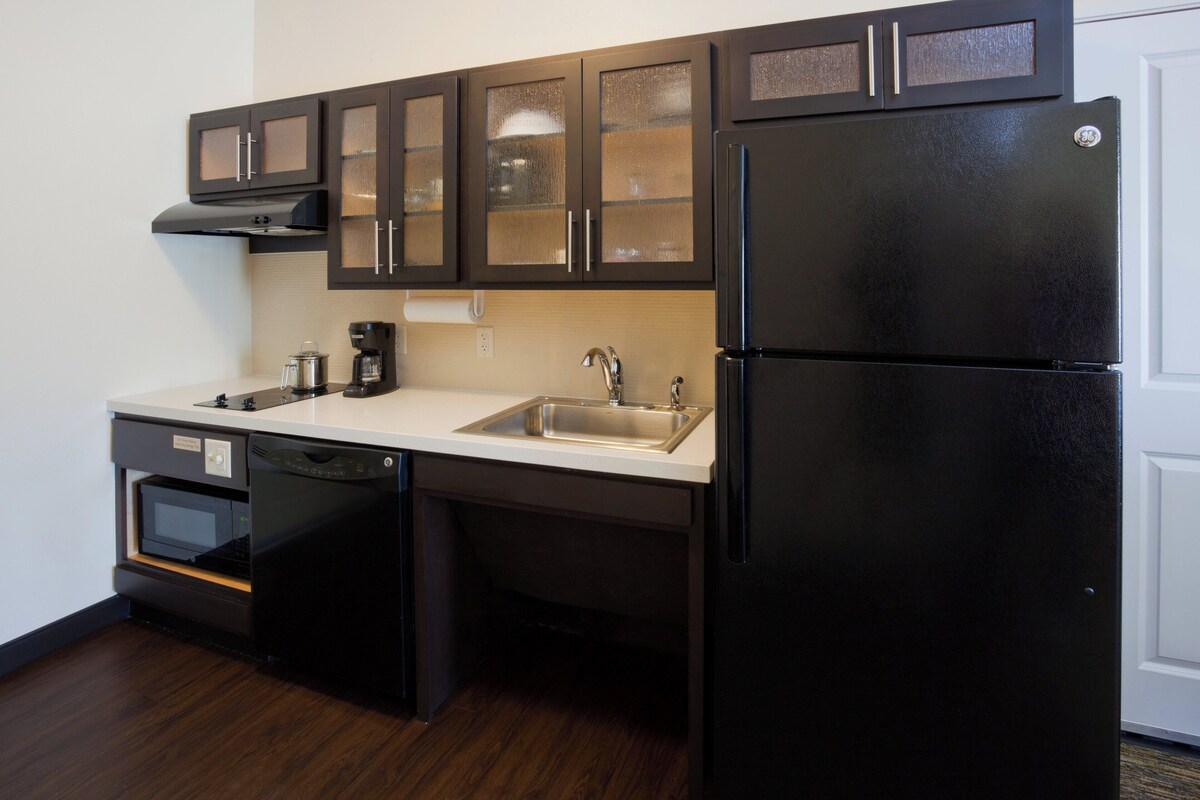 Una cocina con alacenas de madera oscura, un refrigerador negro, un horno empotrado y un lavavajillas.