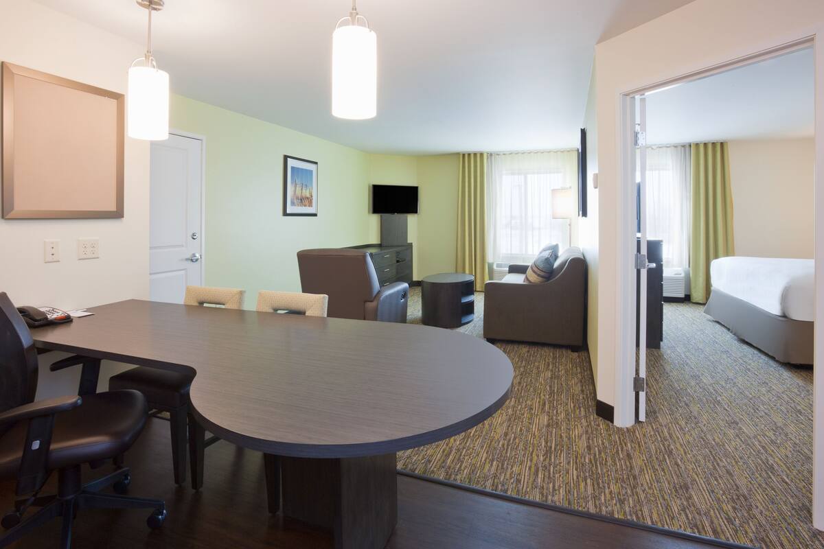 A hotel room with a large desk, two chairs, a sofa, a television, and a bed.