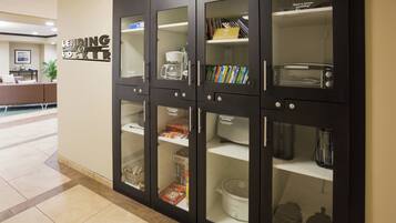 Una biblioteca con armarios de vidrio que contienen libros, juegos de mesa y una máquina de café.