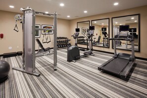 Une salle de sport équipée de divers appareils d’exercice, notamment un tapis de course, un vélo elliptique et des appareils de musculation.