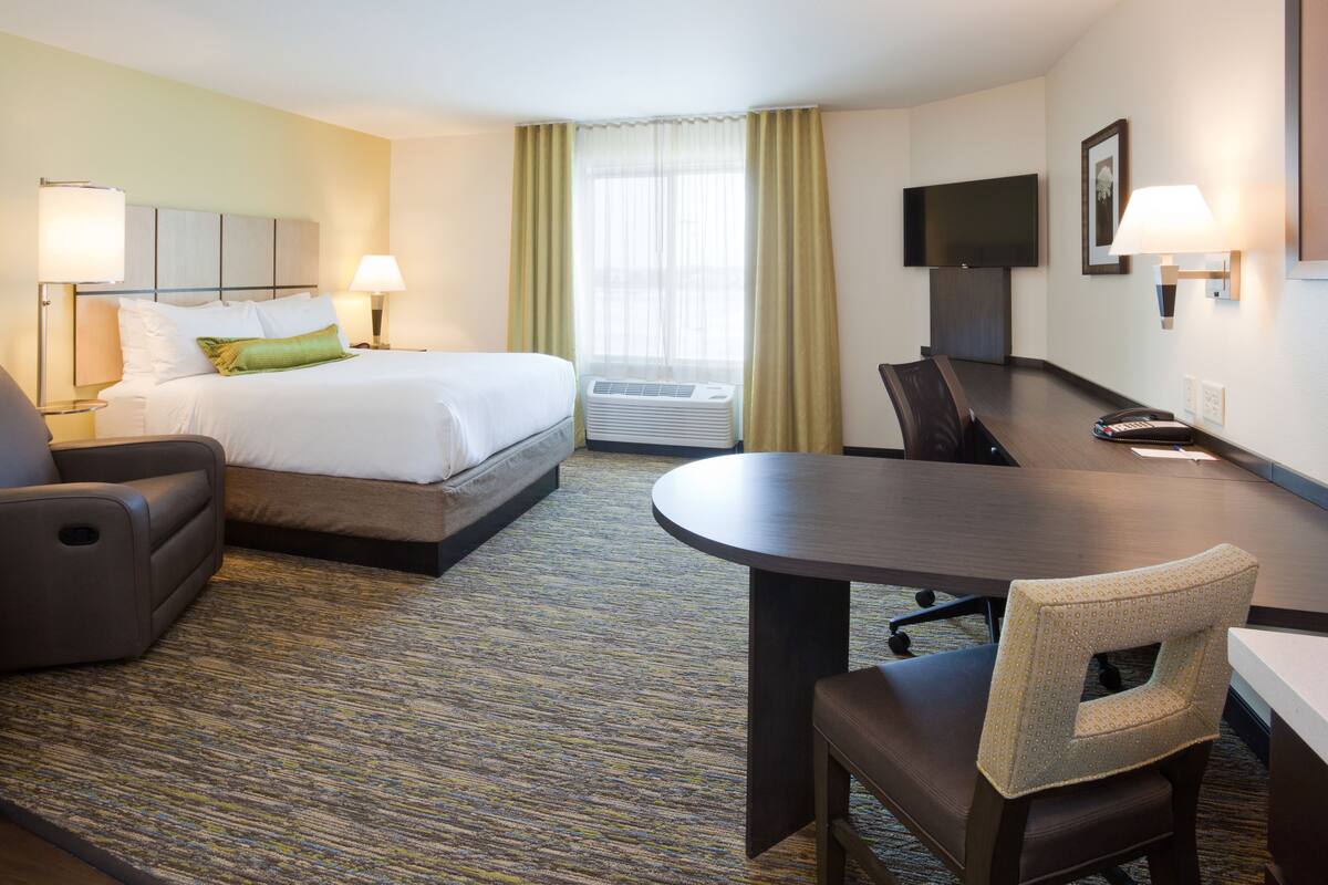 A hotel room with a bed, a desk, a chair, a TV, and a window with curtains.