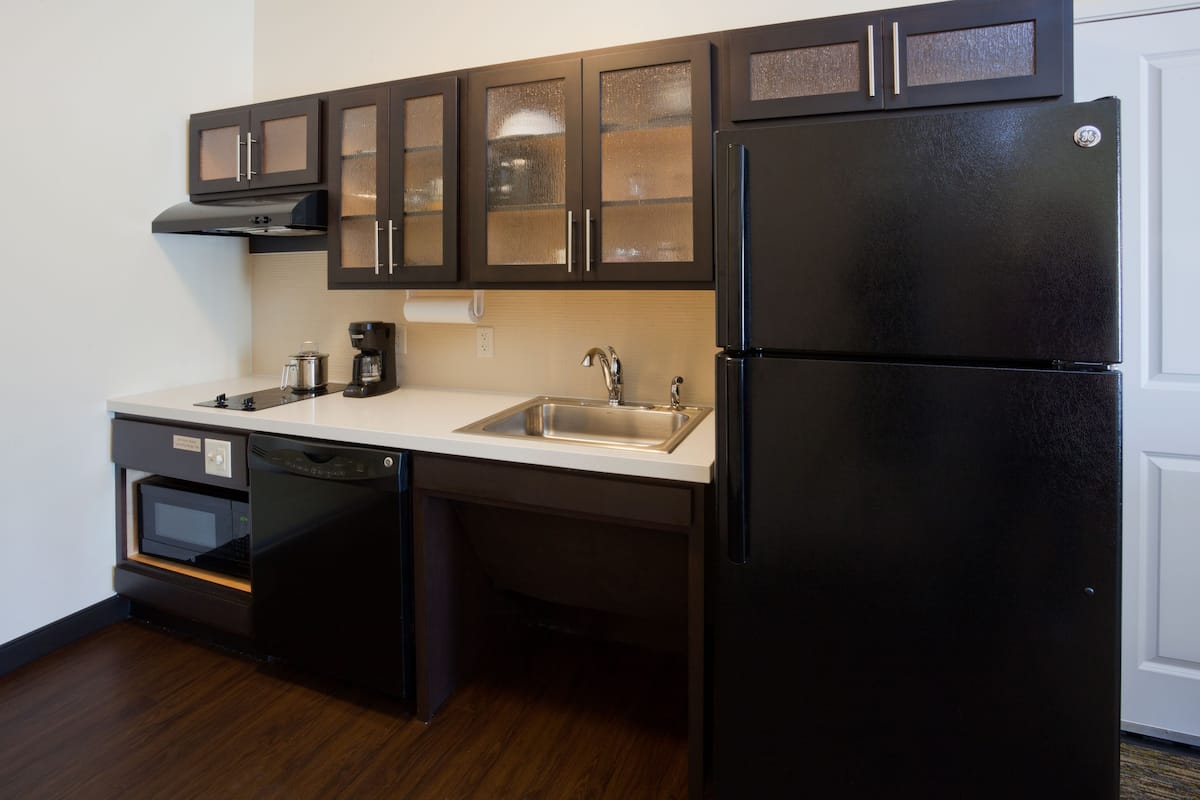 A compact kitchen with dark wooden cabinets, a black refrigerator, a built-in oven, and a dishwasher.