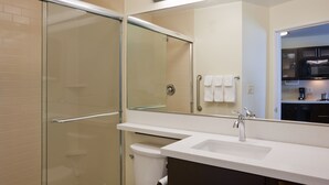 A modern bathroom with a glass-enclosed shower, a white sink, and a mirror reflecting a kitchen area.